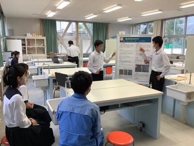 メンターや他のメンバーを前にポスター発表する生徒たち